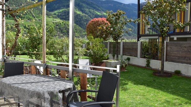 Un patio al aire libre con una mesa y sillas, rodeado por una cerca de madera, con vistas a un paisaje verde y exuberante con colinas al fondo.
