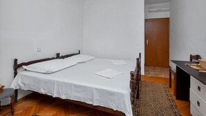 A bedroom with a wooden bed, white bedding, a desk with a chair, and a patterned rug. - Villa Paško - Double room with Balcony and Sea View (Podgora)