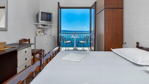 A hotel room with a bed, a desk with a television, a small refrigerator, and a balcony with a table and chairs. - Villa Paško - Double room with Balcony and Sea View (Podgora)