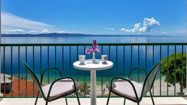 A balcony with a table and chairs overlooking a calm sea with clear skies. - Villa Paško - Double room with Balcony and Sea View (Podgora)