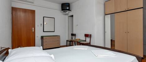 A bedroom with a bed, a dresser, a chair, a small table, a television, and a wardrobe.
