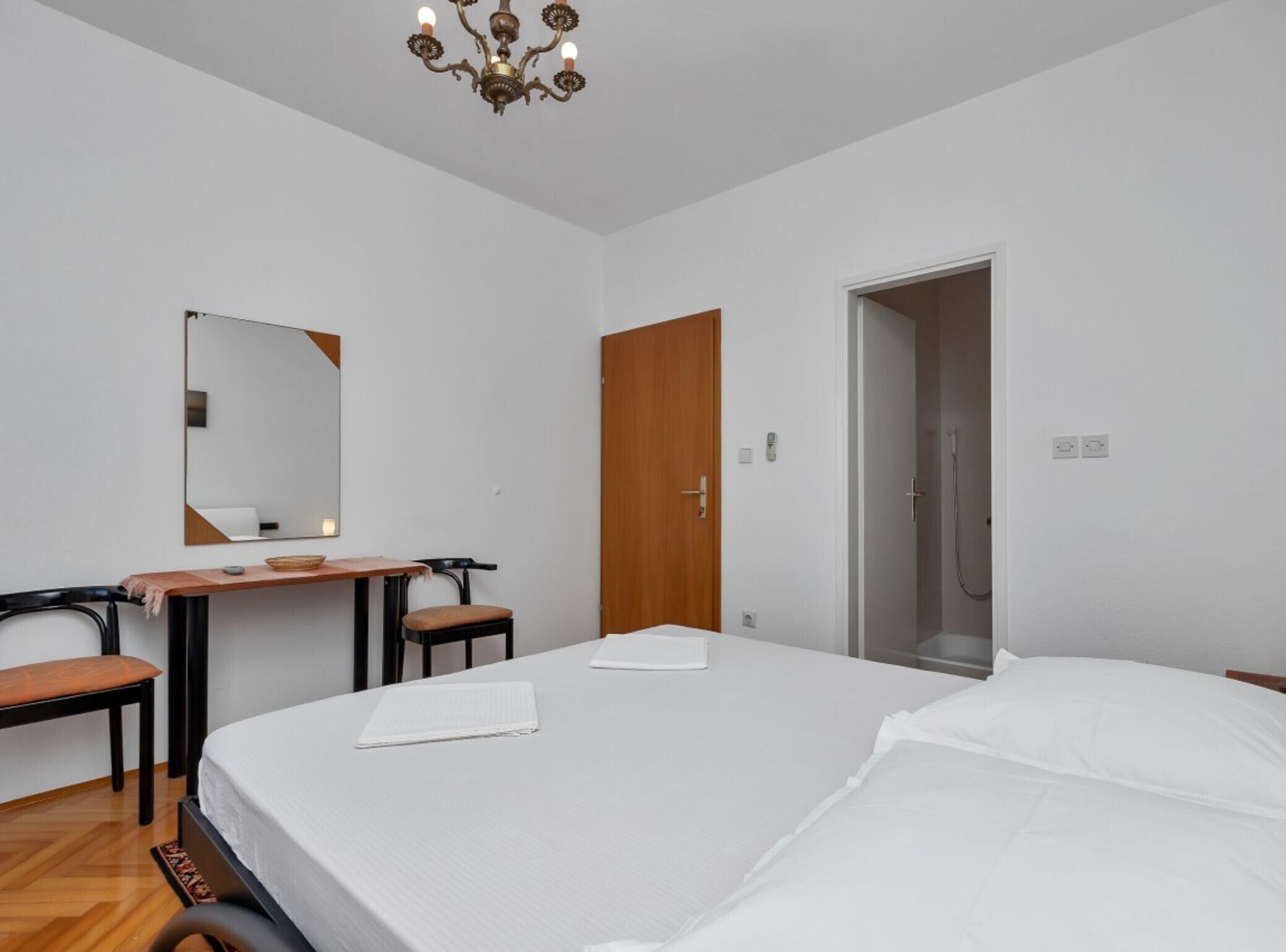 A modern hotel room with a large bed, a desk with two chairs, a wooden door, and a shower area.