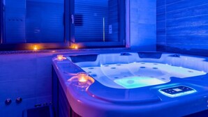 A modern spa area with a hot tub, candles, and a view through large windows.