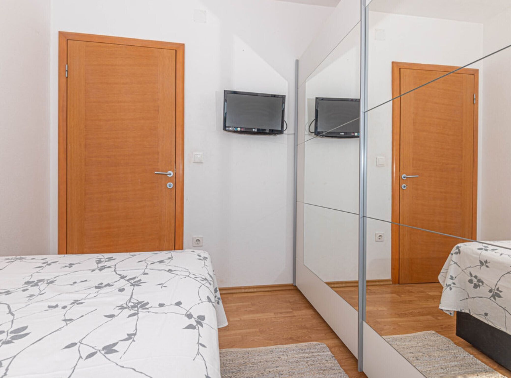 Un dormitorio con cama, televisor montado en la pared y un armario con espejo.