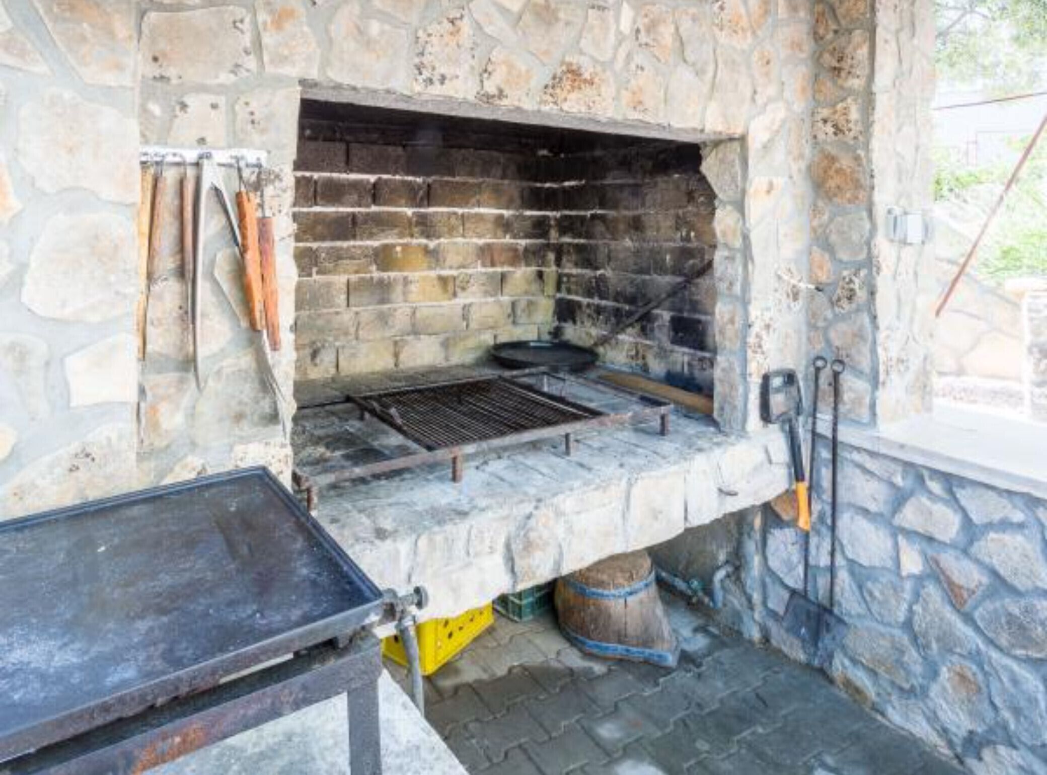 Uma área de cozinha ao ar livre construída em pedra, com churrasqueira e utensílios de cozinha.