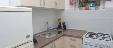 Cocina compacta con refrigerador, lavamanos, estufa y armarios.