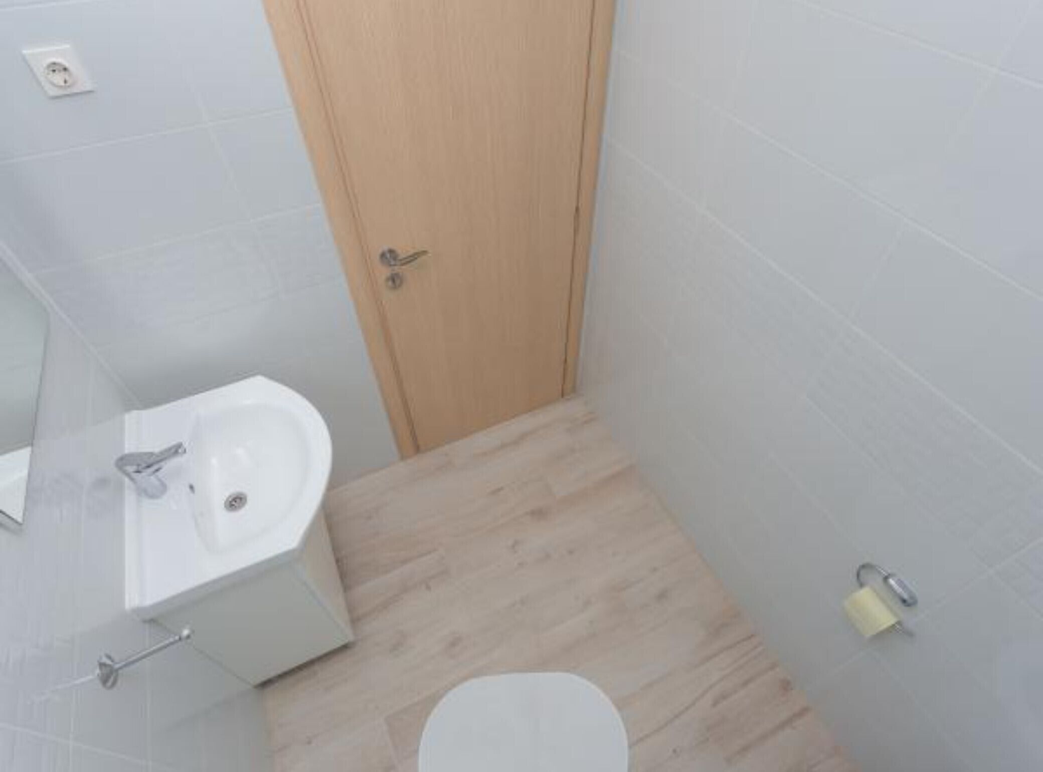 A small bathroom with a wooden door, a white sink, and a toilet.
