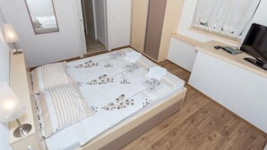 Un dormitorio pequeño y ordenado con cama, mesita de noche, lámpara y ventana con cortinas.