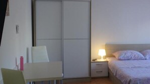 Un dormitorio con cama, mesita de noche, lámpara, silla y armario.