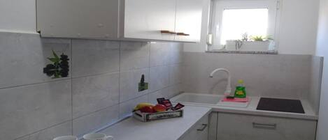 A small kitchen with white cabinets, a countertop, a sink, and a window above it.