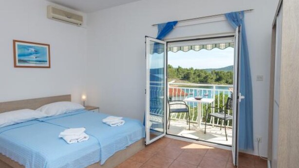 A bedroom with a bed, a small table with a chair, and a balcony with a view of the landscape.