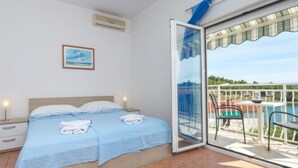A bedroom with a bed, a nightstand, a window with a view of a pool and greenery, and an air conditioning unit.