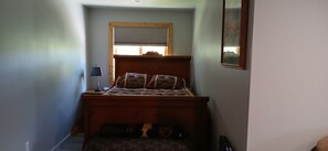 Un dormitorio con cama, mesita de noche, lámpara y ventana con persianas.