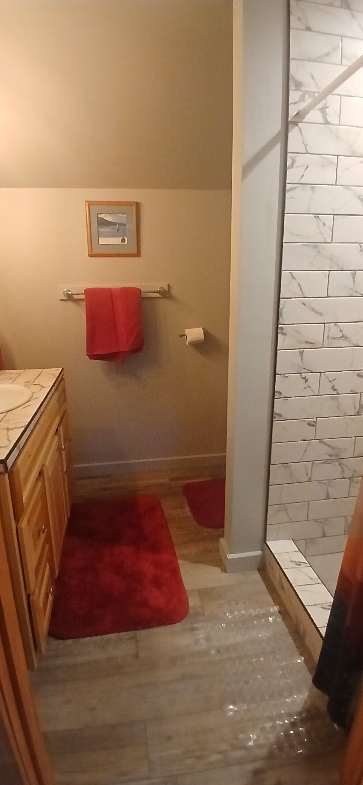 A bathroom with a marble wall, wooden cabinets, a red towel, and a small framed picture on the wall.