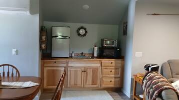 Una cucina compatta con mobili in legno, un frigorifero, un forno a microonde e un tostapane. C'è un tavolo da pranzo con sedie e un tappeto piccolo.
