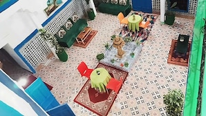 Um pátio com piso estampado, paredes verdes e azuis, uma pequena fonte e área de estar ao ar livre.