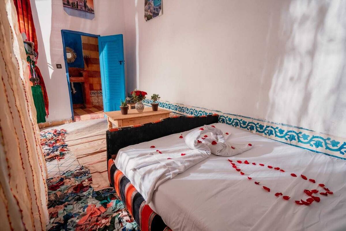 A room with a bed, a wooden table, and a blue door.