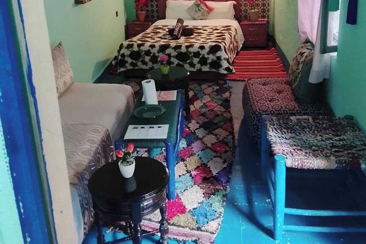 A bedroom with a bed, a sofa, a small table, and a hanging plant.