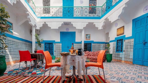 Um pátio com área de refeições, apresentando uma mesa posta para dois, rodeada por cadeiras e um tapete decorativo.