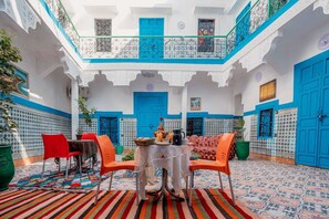 A courtyard with a dining area featuring a table set for two, surrounded by chairs, and a decorative rug. - Riad dar Medina Land (Marrakech)