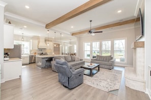 A spacious living room with a grey recliner, a grey sofa, and a coffee table. There is a fireplace and a TV mounted on the wall.