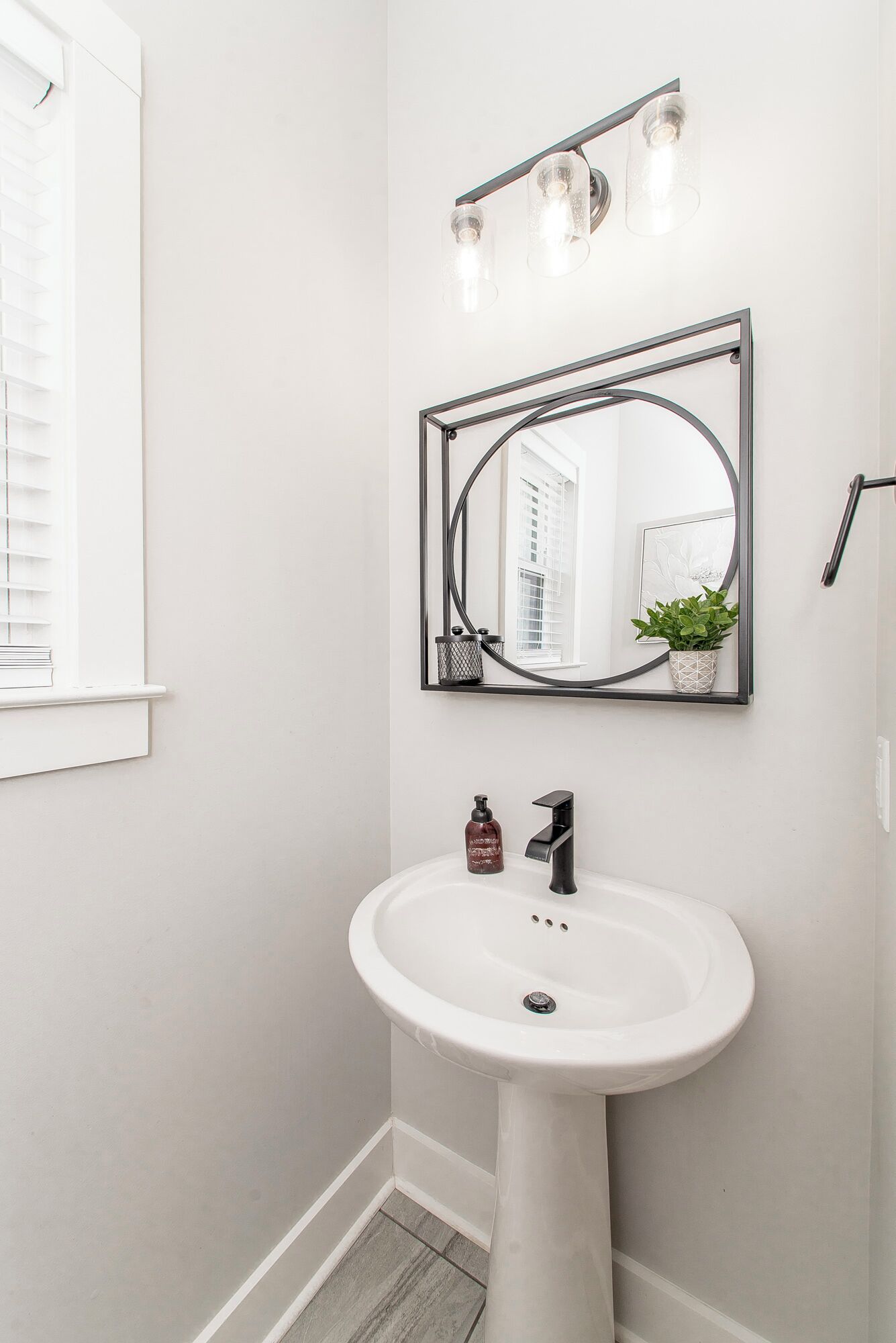 Un bagno con lavandino bianco, specchio e finestra con persiane.