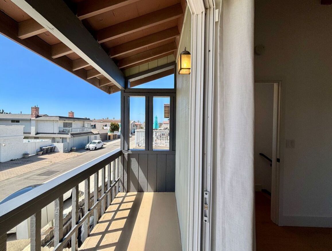 A balcony with a view of a street and buildings, a door, and a window with a light fixture.