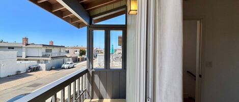 A balcony with a view of a street and buildings, a door, and a window with a light fixture.