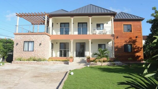 A two-story house with a balcony, a stone facade, and a well-maintained lawn.