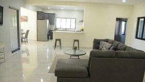 A modern living room with a sectional sofa, a round coffee table, and a dining area with two stools.