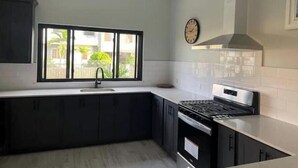 A modern kitchen with dark cabinets, a large window, a stove, and a clock on the wall.
