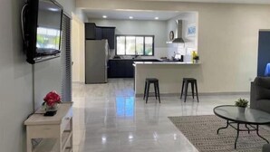 A modern kitchen with a built-in oven, a refrigerator, and a window. There is a dining area with a glass table and two bar stools.