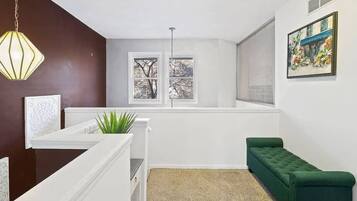 A room with a white reception desk, a green bench, a plant, and a window with a view of trees.