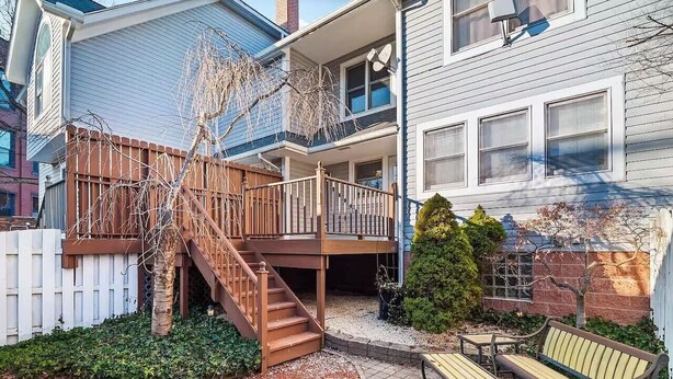A two-story house with a wooden staircase leading to a balcony, a fenced garden area, and outdoor seating. - Fun 3 BR Home in Ohio City | Game Room | Sleeps 11 (Cleveland)