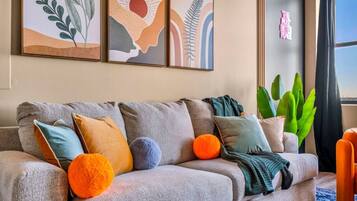 A living room with a grey sofa, colorful cushions, and abstract wall art.