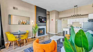A modern living room with a fireplace, dining area with yellow chairs, and a kitchen with white cabinets.