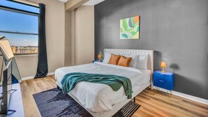 A modern bedroom with a large bed, a desk, and a view of the city. - Colorful 2Bed Apt • Heart of Downtown • Lake Views (Cleveland)