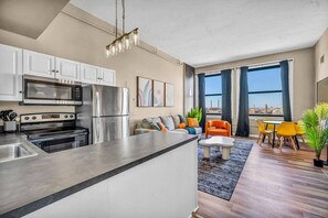 A modern kitchen with stainless steel appliances, a dining area with yellow chairs, and a view of the city through large windows.
