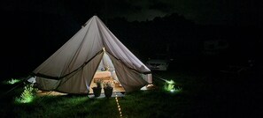 A tent set up in a grassy area at night with a vehicle parked nearby.