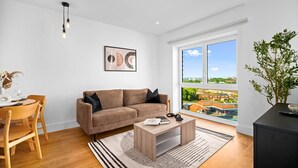 Ein modernes Wohnzimmer mit einem braunen Sofa, einem Holzespeisetisch und Stühlen. Es gibt ein großes Fenster mit Blick auf eine Stadtansicht.