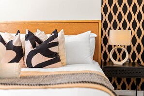 A neatly made bed with a patterned throw, a bedside table with a lamp, and a wall with a geometric pattern. - Stylish Apartment * Balcony * Fast WiFi * Netflix (Birmingham)