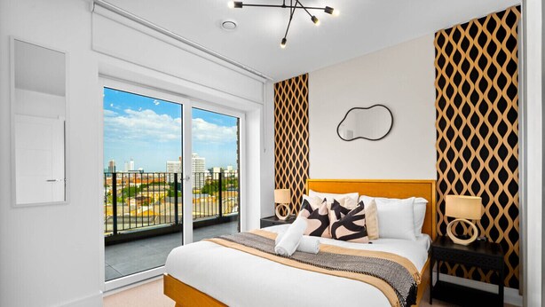 Ein modernes Schlafzimmer mit einem großen Bett, einem Nachttisch, einer Wandlampe und Blick auf die Stadt durch eine Schiebetür.