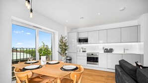 Una cucina moderna con mobili bianchi, elettrodomestici in acciaio inossidabile e un'area pranzo con tavolo e sedie in legno.