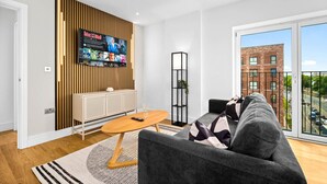 Un soggiorno moderno con un divano grigio, un tavolino in legno e una TV montata su una parete rivestita in legno.