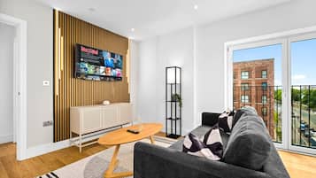 A modern living room with a grey sofa, a wooden coffee table, and a TV mounted on a wooden panel wall.