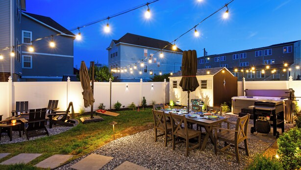 Een terras buiten met lichtslingers, een barbecuegrill en een eettafel met stoelen.