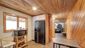 Une cuisine compacte avec des meubles de rangement en bois, un réfrigérateur, un four à micro-ondes et une petite table à manger.