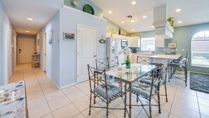Cocina moderna con armarios blancos, una isla central y un comedor con sillas de metal y una mesa de vidrio.