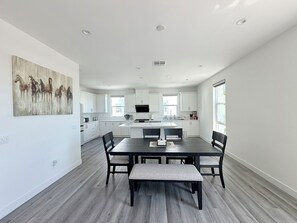 Cocina moderna con armarios blancos, una isla central y una zona de comedor con una mesa y sillas de madera oscura.