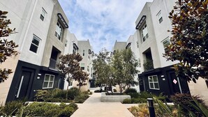 A modern residential building with a central courtyard, featuring a symmetrical design with two-story structures, a paved walkway, and surrounding greenery.